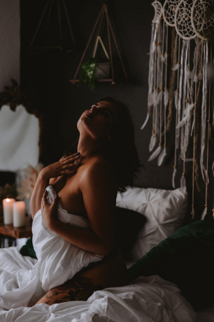 Boudoir Photographer, woman sits up in bed with covers pulled up